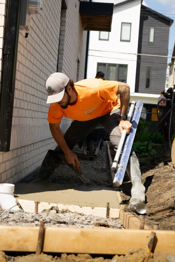 Construction worker smoothing freshly poured concrete near a building.