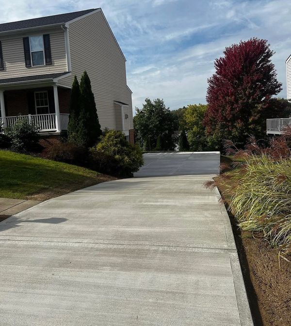 A suburban driveway leading to a garage with autumn foliage around.