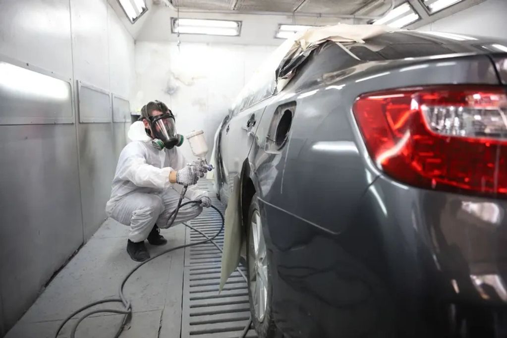 Worker spray painting a grey car in a workshop.