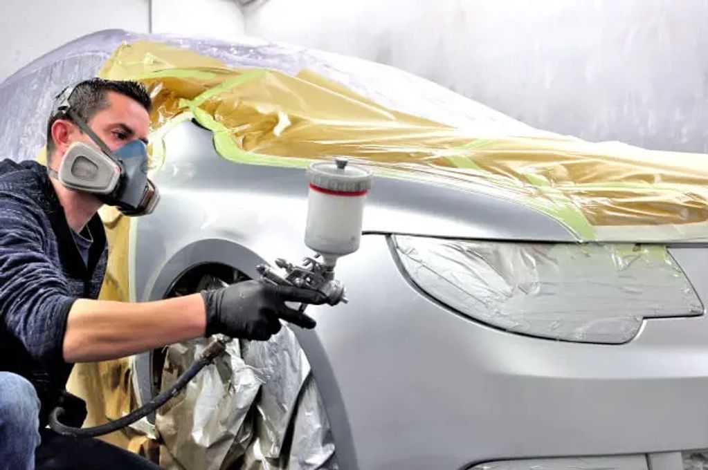 Person spray painting a car while wearing a mask.
