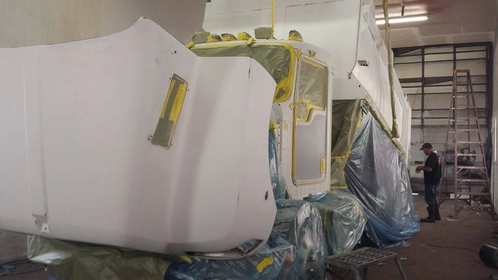 Truck undergoing a paint job with protective masking in a workshop.