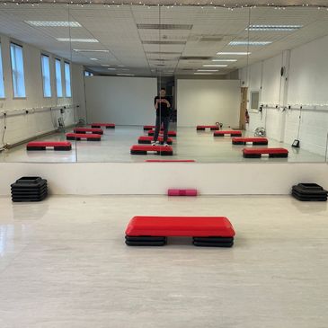 Empty fitness studio with red step platforms and mirrored wall.