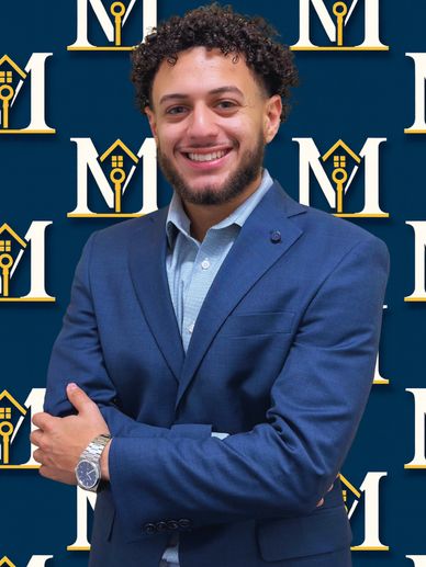Confident man in a blue suit smiles against a branded backdrop.