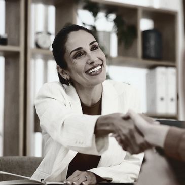 A smiling woman in a white blazer shaking hands with another person. Locum recruiter