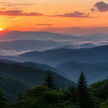 Sunset over misty mountain ranges with vibrant orange sky.