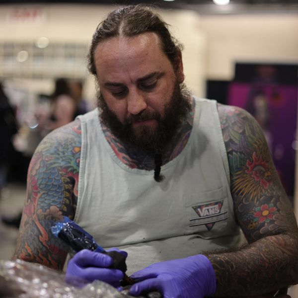 Tattoo artist with colorful sleeves focused on his work, wearing purple gloves.