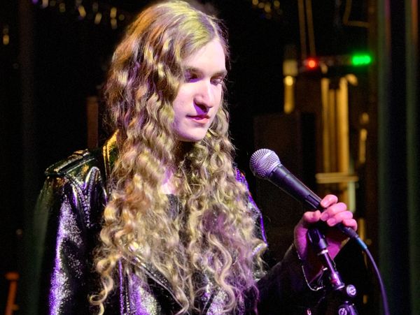 Person with long curly hair holding a microphone on stage.