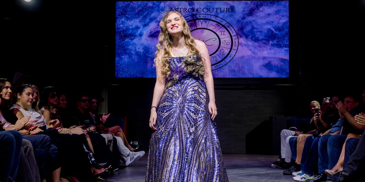 Model walks runway in a sparkling purple gown at a fashion show with applause.