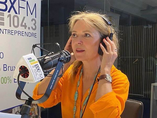 A woman in an orange shirt is talking into a microphone.