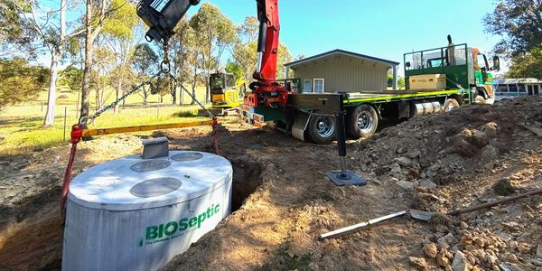 A truck with a crane is installing a BIOseptic tank in a rural area.
