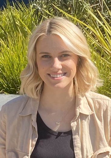 Smiling woman with blonde hair outdoors in sunlight.