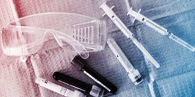 Laboratory safety glasses with syringes and test tubes on a blue cloth.