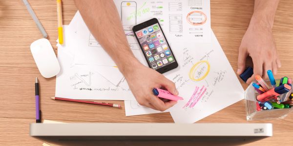 Person highlighting notes on design sketches with phone and pens nearby.