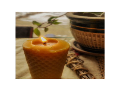 A lit honeycomb candle with a plant and pot in the background.