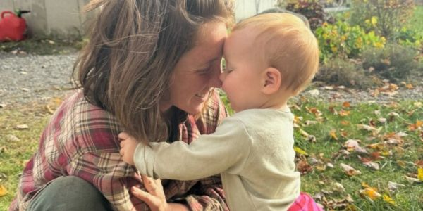 Woman and toddler touching foreheads outdoors.