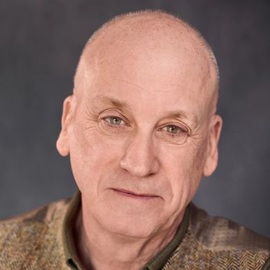 Smiling older man with bald head and textured jacket.