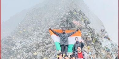 Group of hikers posing with Indian flag on a misty rocky mountain peak.