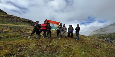 Group of hikers holding Indian flag on a misty mountain slope.