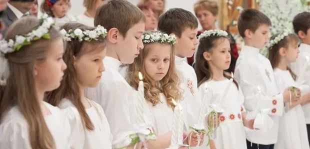 Children in white attire holding candles, likely during a religious ceremony.