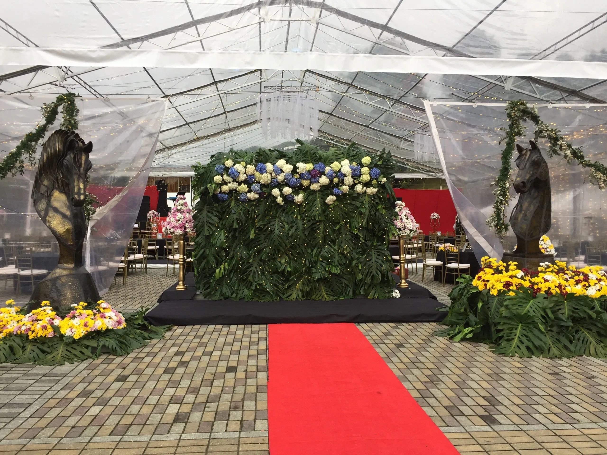 Elegant floral and horse head statues under a transparent tent with fairy lights.