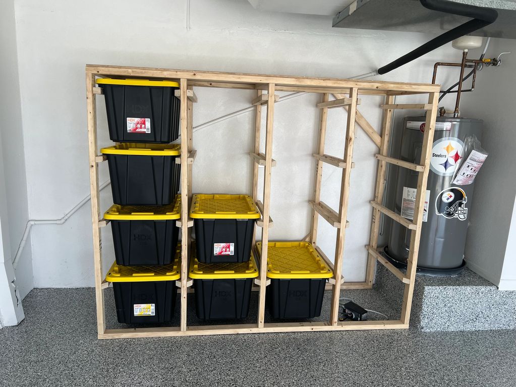 Wooden shelving unit with black and yellow storage bins beside a water heater.