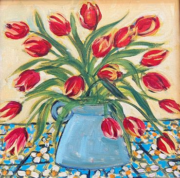 Red tulips in a blue vase on a patterned table.