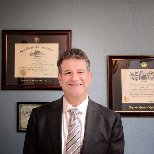 Man in suit standing in front of framed certificates.