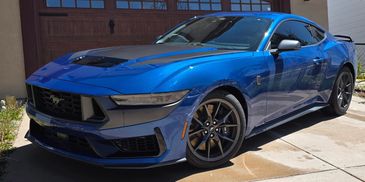 Sleek blue Ford Mustang parked outside a garage on a sunny day.