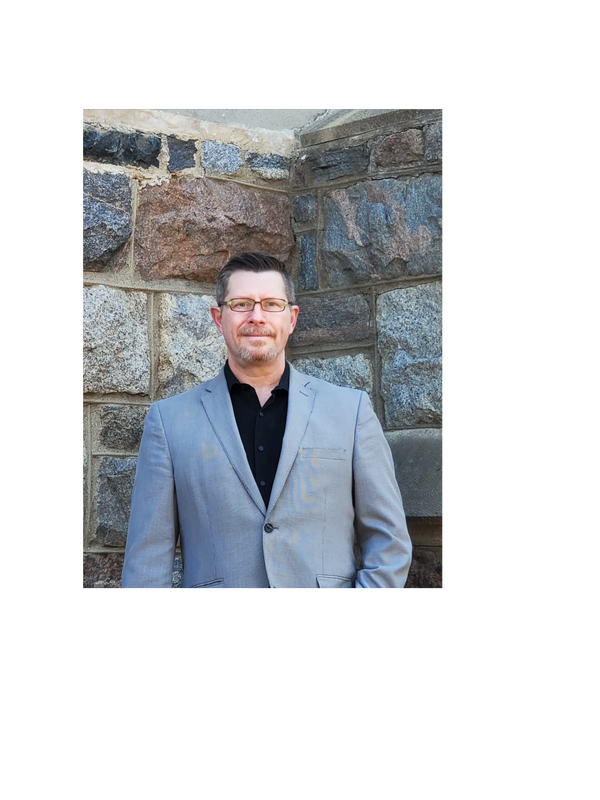 Archeologist, Alan Korejbo, is standing in front of an historic stone building. He is looking at the