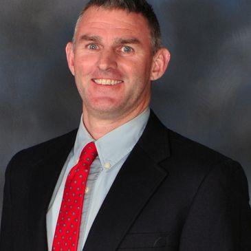 Smiling man in a suit with a red tie against a gray backdrop.