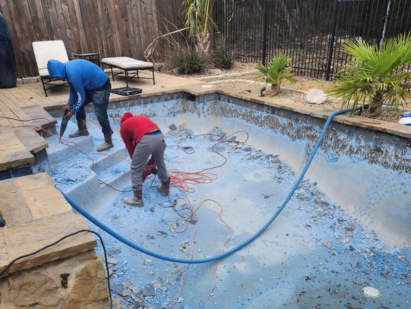 Workers renovating an empty pool by chipping away old paint.