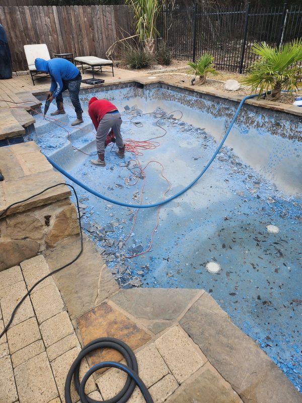 Workers renovating an empty pool by chipping away old paint.