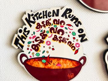 A sign saying 'This Kitchen Runs On' with Malayalam words and a cooking pot illustration.