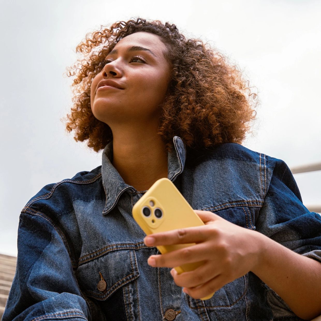 Woman holding a yellow phone looking upwards.