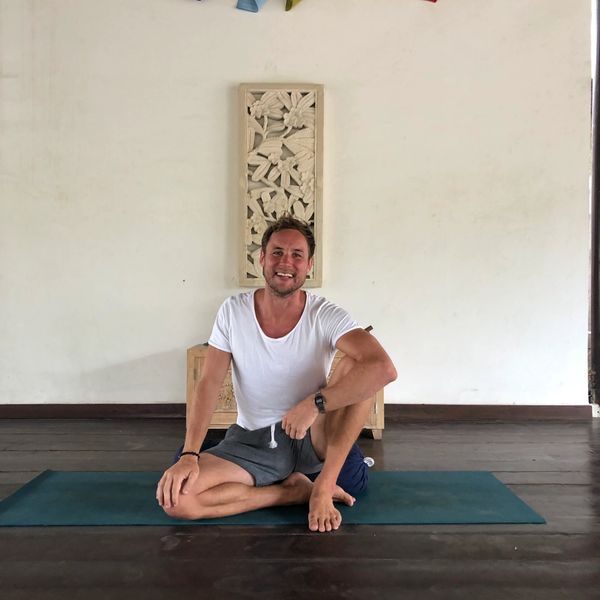Man sitting cross-legged on a yoga mat indoors, smiling.