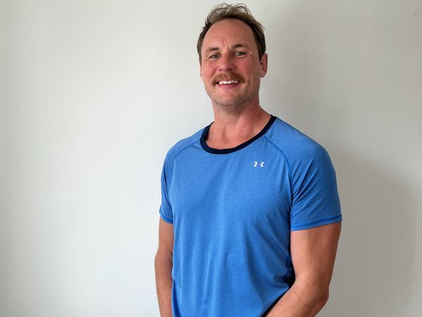 Man in blue athletic shirt smiling against a plain wall.