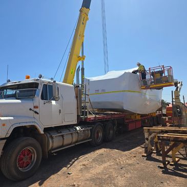 Worker inspects large wrapped cargo on a flatbed truck using a lift under clear blue sky.