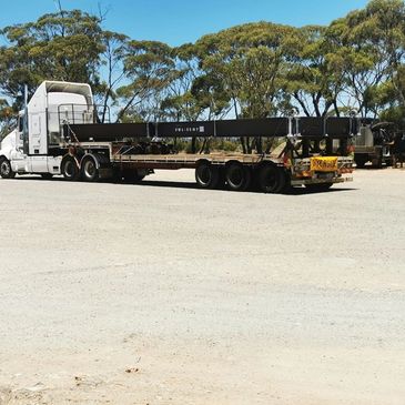 A large white truck with an oversized load sign parked on a dirt road under blue sky.