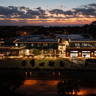 Aerial view of a lit commercial complex at dusk with a colorful sunset sky.