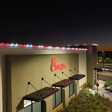 Chick-fil-A restaurant illuminated at dusk with festive red and white lights.