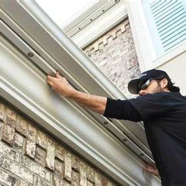 A man installs a gutter on a brick house exterior.
