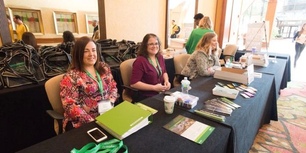 Three women sitting at a registration table with materials and badges.