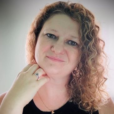 Woman with curly hair and a gentle smile resting her chin on her hand.