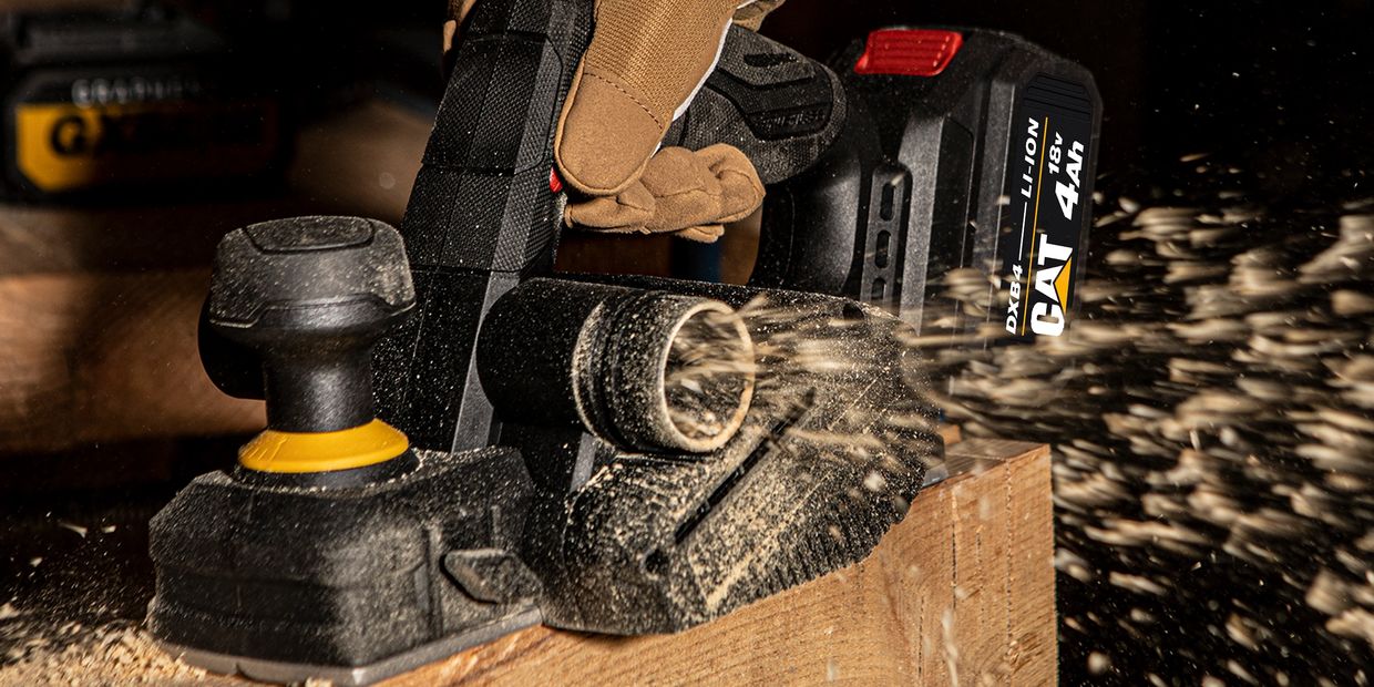 A power planer smoothing wood with flying sawdust.
