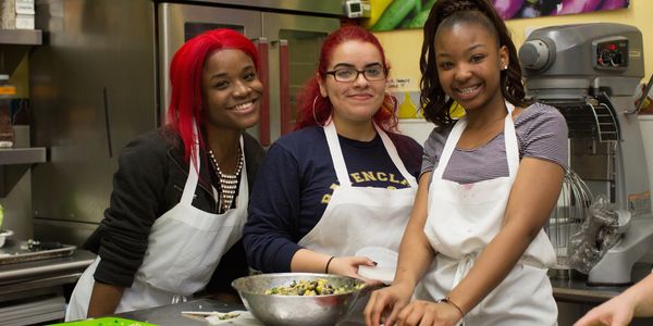 Three smiling young women cooking together in a kitchen.