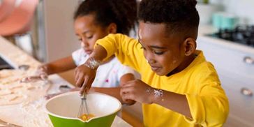 Two children happily baking together, mixing ingredients in a bowl.