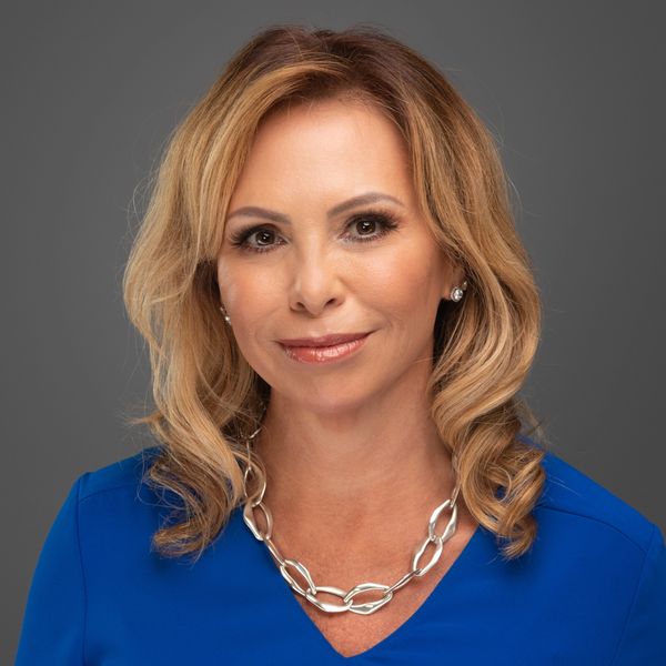 Confident woman with blonde hair wearing a blue top and silver chain necklace.