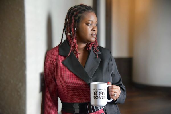 "Capricia Griffin holding a cup that says 'Be careful or you'll end up in my novel,' with a playful expression."