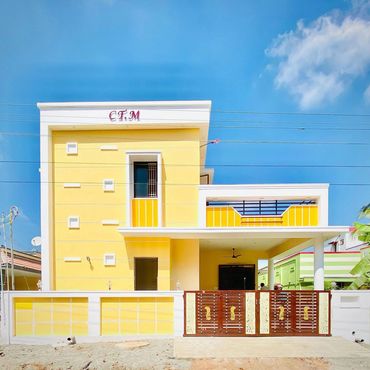 Bright yellow two-story house with a decorative brown gate under a clear blue sky.