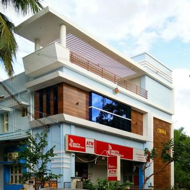 Modern building housing South Indian Bank ATM with a brown car and motorcycle parked outside.